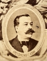 Fotografie w odcieniu sepii umieszczone na tle drzew i roślin, w centralnym miejscu postać kobiety ze sztandarem i aniołkami, wkomponowane widoki budowanej stacji, mostu kolejowego i lokomotywy. Największe zdjęcie w górnej, środkowej części bez podpisu, prawdopodobnie inż. głównej kolei nadwiślańskiej Tadeusz Chrzanowski lub jego następca Walery Titkow. Wśród podobizn pracownicy Biura Głównego Inżyniera: inż. Włodzimierz Stanisławski - pomocnik głównego inżyniera; inż. Feliks Kucharzewski -  pomocnik naczelnika biura; Feliks Kamocki - naczelnik kancelarii; Witold Lanci - naczelnik Wydz. Architektury; dr Wacław Lasocki- służba zdrowia; Władysław Radwan - sprawy zakupu gruntów; inż. Stanisław hr Scipio - projektant mostów kolejowych i jego współpracownicy: inż. Stefan Zieliński, inż. Maurycy Machalski, inż. Feliks Kucharzewski. Fotografia w passe - partout, za szkłem, oprawiona w drewnianą, profilowaną ramę.