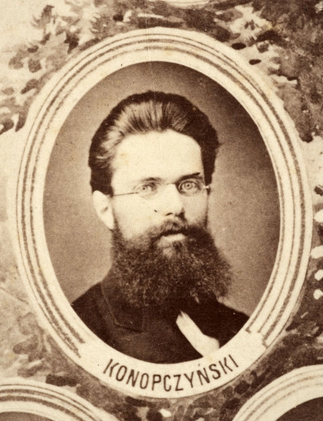 Fotografie w odcieniu sepii umieszczone na tle drzew i roślin, w centralnym miejscu postać kobiety ze sztandarem i aniołkami, wkomponowane widoki budowanej stacji, mostu kolejowego i lokomotywy. Największe zdjęcie w górnej, środkowej części bez podpisu, prawdopodobnie inż. głównej kolei nadwiślańskiej Tadeusz Chrzanowski lub jego następca Walery Titkow. Wśród podobizn pracownicy Biura Głównego Inżyniera: inż. Włodzimierz Stanisławski - pomocnik głównego inżyniera; inż. Feliks Kucharzewski -  pomocnik naczelnika biura; Feliks Kamocki - naczelnik kancelarii; Witold Lanci - naczelnik Wydz. Architektury; dr Wacław Lasocki- służba zdrowia; Władysław Radwan - sprawy zakupu gruntów; inż. Stanisław hr Scipio - projektant mostów kolejowych i jego współpracownicy: inż. Stefan Zieliński, inż. Maurycy Machalski, inż. Feliks Kucharzewski. Fotografia w passe - partout, za szkłem, oprawiona w drewnianą, profilowaną ramę.