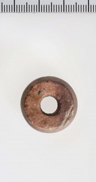 wykonany z łupka owruckiego; dwustożkowy, ostro profilowany; linia tworząca kształt dwustożkowy biegnie nieregularnie na różnych wysokościach; płasko ścięty przy otworze; otwór średniej wielkości, cylindryczny