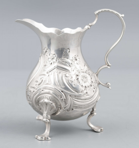 S/Mt/581/ML - Korpus o kształcie gruszkowatym, z wydłużonym wylewem, na trzech nóżkach, ucho profilowane. Krawędź wylewu wycięta faliście, korpus repusowany: na froncie rocaillowy kartusz, po bokach ornamenty wolutowe i kwiatowe.
Na spodzie znaki:
- urząd probierczy w Londynie
- próba Sterling
- oznaczenie roku 