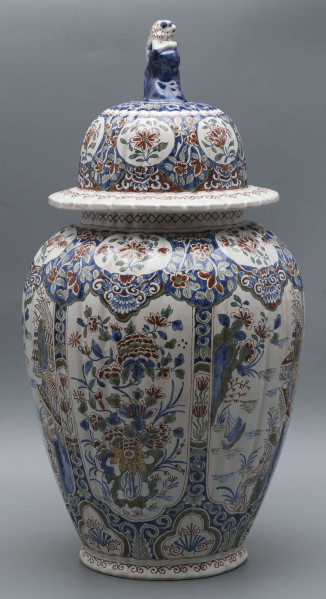 S/CS/546/ML - Wazon owoidalny o niskiej podstawie i niskiej pierścieniowej szyi, powierzchnia drobno kanelowana, pokrywa kopulasta z szerokim kołnierzem, uchwyt w kształcie lwa Fo wspartego prawą łapą na pniu drzewa (?). Dekoracja malowana podszkliwnie w kolorach błękitu, czerwieni, zieleni, żółcieni. W sześciu owalnych, wydłużonych rezerwach na przemian kompozycja kwiatowa z peonią i pejzaż nadrzeczny z architekturą o charakterze orientalnym. U góry - na barkach - sześć owalnych rezerw z kwitnącą gałązką, na dole sześć rezerw trójlistnych z motywem uproszczonej muszli i wolut, na stopie fryz wolutowy, na szyi wąska ukośna kratka. Na pokrywie powtórzona dekoracja z barków, kołnierz biały z fryzem wolutowym analogicznie jak na stopie.
 