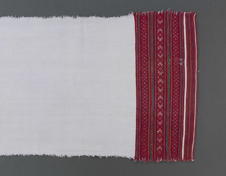 Ręcznik z samodziałowego płótna tkanego splotem prostym. Brzegi dolne, na szer. 14,5 cm, ozdobione ornamentem tkackim zw. pereborami. Ułożony pasowo, złożone z motywów geometrycznych w postaci rombów, kształtów litery X oraz drobnych prążków, w kolorze niebieskim, pomarańczowym i czerwonym.