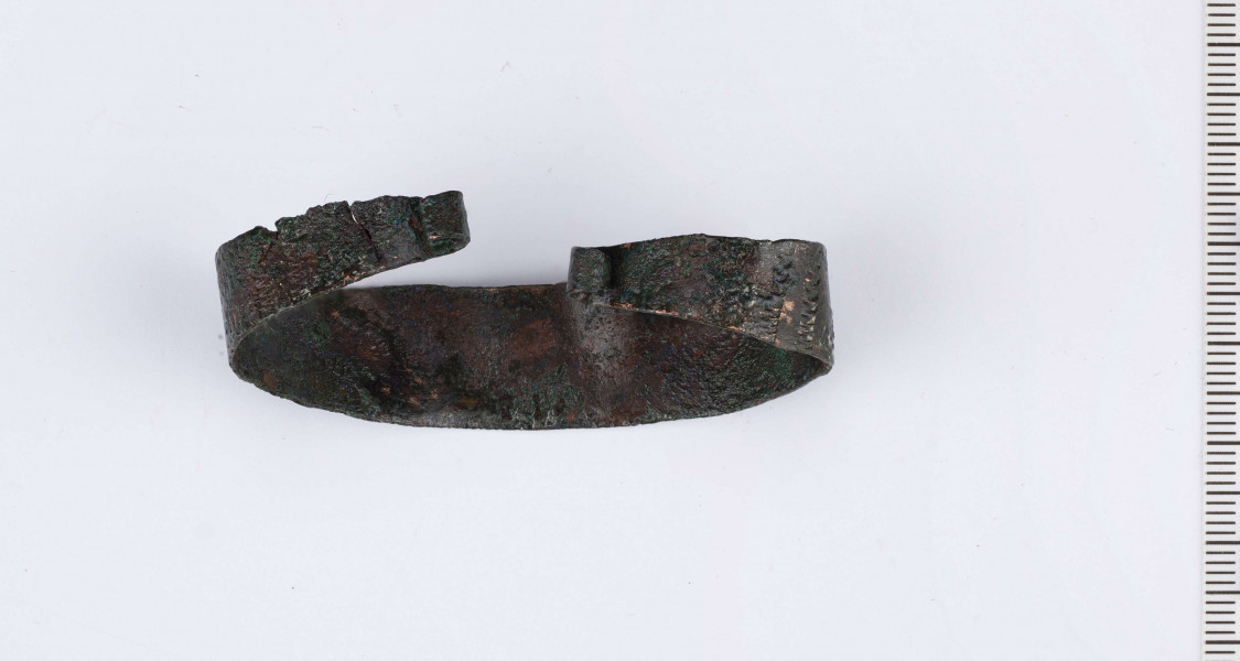 Bransoleta brązowa wykonana z płaskiej taśmy zwężającej się ku końcom.
