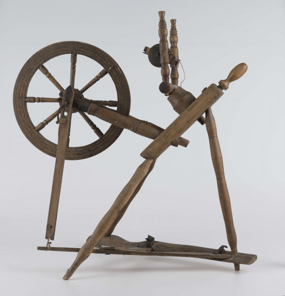 E/16647/ML - Kołowrotek poziomy, drewniany, ozdobnie toczony. Drewno niemalowane. Podstawa to 3 skośnie ustawione nóżki. Dwie z nich osadzone w wąskiej listwie. Górne końce nóżek osadzone w prostokątnej pochyłej grubej desce (11 x 32 x 4 cm). Stanowi ona podstawę do osadzenia koła napędowego i szpuli zwijającej nici. W niej zamocowany uchwyt połączony ze śrubą, która reguluje położenie szpuli. Koło osadzone na metalowej ośce posiada 8 toczonych ozdobnie szprych. Jeden koniec ośki połączony pionową ruchomą listewką z pedałem wprawiającym w ruch kołowrotek. Szpula osadzona również na metalowej ośce.