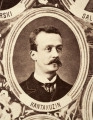 Fotografie w odcieniu sepii umieszczone na tle drzew i roślin, w centralnym miejscu postać kobiety ze sztandarem i aniołkami, wkomponowane widoki budowanej stacji, mostu kolejowego i lokomotywy. Największe zdjęcie w górnej, środkowej części bez podpisu, prawdopodobnie inż. głównej kolei nadwiślańskiej Tadeusz Chrzanowski lub jego następca Walery Titkow. Wśród podobizn pracownicy Biura Głównego Inżyniera: inż. Włodzimierz Stanisławski - pomocnik głównego inżyniera; inż. Feliks Kucharzewski -  pomocnik naczelnika biura; Feliks Kamocki - naczelnik kancelarii; Witold Lanci - naczelnik Wydz. Architektury; dr Wacław Lasocki- służba zdrowia; Władysław Radwan - sprawy zakupu gruntów; inż. Stanisław hr Scipio - projektant mostów kolejowych i jego współpracownicy: inż. Stefan Zieliński, inż. Maurycy Machalski, inż. Feliks Kucharzewski. Fotografia w passe - partout, za szkłem, oprawiona w drewnianą, profilowaną ramę.