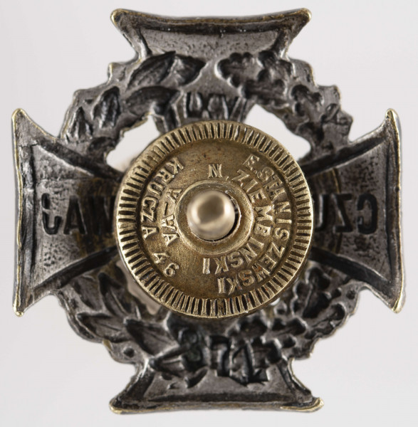 ML/MART/284 - Krzyż harcerski ze złotą lilijką wykonany z metalu, należał do harcerza Stanisława Maciąga. Z tyłu krzyż na zapięcie/nakrętkę. Krzyż harcerski 4-ramienny wykonany z metalu, na środku złota lilijka harcerska w tle liście wawrzynu, na krzyżu napis 