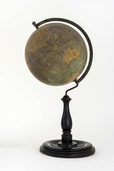 Globus bez tytułu, roku wydania i granic państwowych. Brak hipsometrii, powierzchnia kontynentów jest bladożółta za wyjątkiem białej Antarktydy. Na lądach naniesiono rzeki, pustynie i jeziora zaznaczono szrafurą. Największe góry oznaczono metodą kreskową (za pomocą 