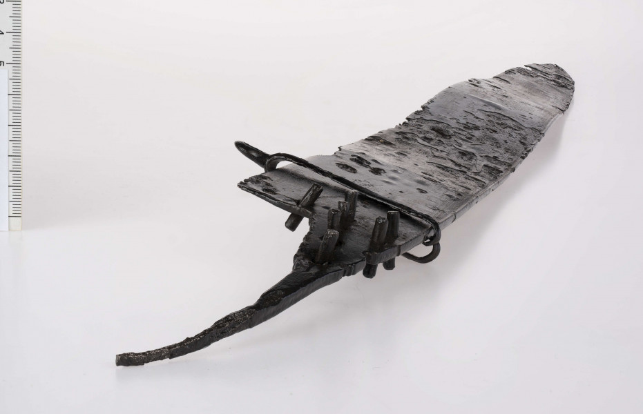 Miecz o chropowatej, poczerniałej powierzchni z wyszczerbionym ostrzem, bez rękojeści.