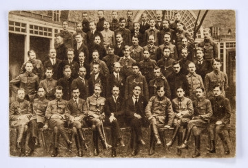ML/H/2177/5 Pocztówka sepiowana - Szkoła Oficerska Polskiej Organizacji Wojskowej w 1916 r. (fotografia pamiątkowa). Ujęcie w poziomie.
AWERS: grupa mężczyzn w mundurach austriackich lub ubraniach cywilnych; pierwszy rząd siedzących, za nimi 5 rzędów stojących; wśród obecnych dwaj lublinianie - Wacław Policzkiewicz (II rząd, 4-ty z prawej) i Jan Arnsztajn (III rząd, 4-ty z prawej); zdjęcie wykonane na tle budynku.
REWERS: czarna linatura z miejscem na korespondencje; w l. g. rogu nadruk w postaci odznaki pamiątkowej