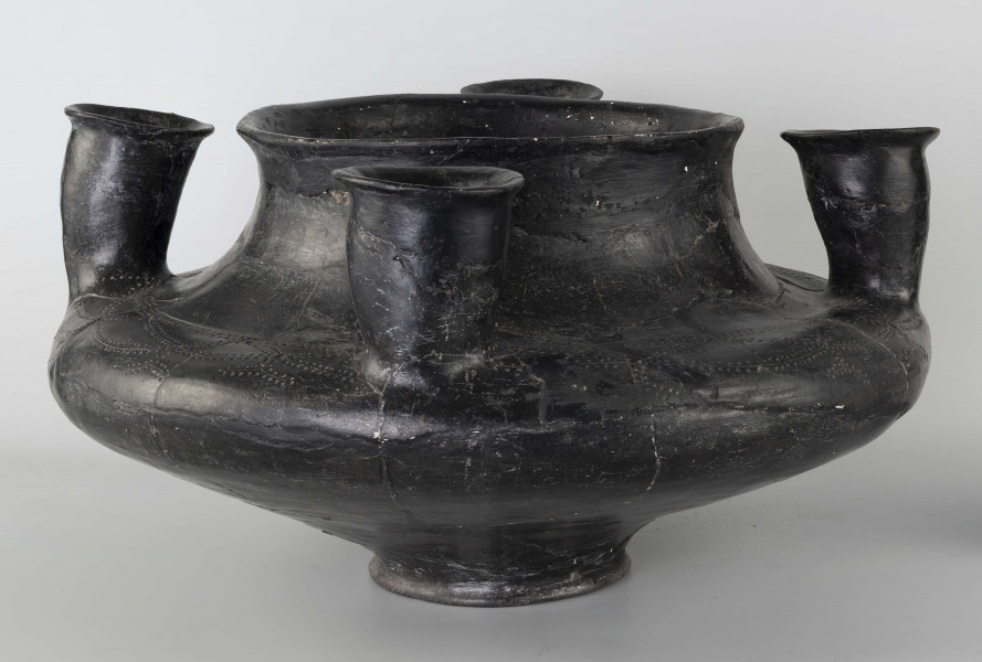 598/A/ML - naczynie kultowe (kernos) kultury pomorskiej; 
wymiary dodatkowe: 25,0 cm - średnica centralnego wylewu
opis: naczynie wazowate o czarnej, błyszczącej powierzchni, którego brzusiec został ozdobiony ornamentem złożonym z linii rytych oraz nakłuć; wokół głównego otworu posiada cztery symetrycznie rozmieszczone kielichy-rytony, które mają nieco wydęte ścianki boczne i kielichowato rozchylone na zewnątrz krawędzie otworów; rytony łączą się z głównym otworem kanalikami; 