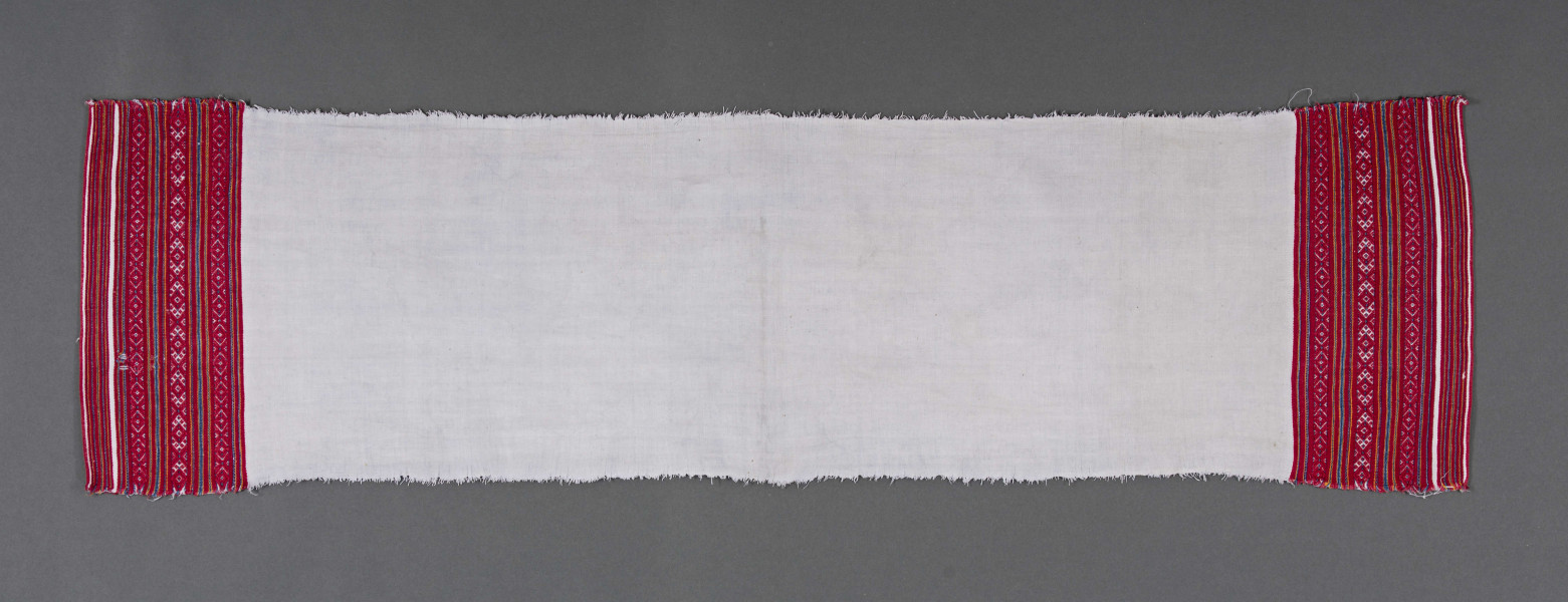 Ręcznik z samodziałowego płótna tkanego splotem prostym. Brzegi dolne, na szer. 14,5 cm, ozdobione ornamentem tkackim zw. pereborami. Ułożony pasowo, złożone z motywów geometrycznych w postaci rombów, kształtów litery X oraz drobnych prążków, w kolorze niebieskim, pomarańczowym i czerwonym.