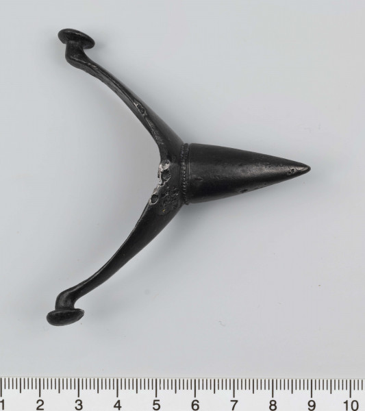 1044/A/ML/1 - Ostroga żelazna z wklęsłym do wewnątrz, łukowatym kabłąkiem. Szeroki przy nasadzie kolca kabłąk zwęża sie stopniowo, przechodząc w wałkowate wygięcia zaczepu, zakończone soczewkowatymi guzkami. Kolec częściowo pusty, ma kształt przegiętego nieznacznie, facetowanego stożka. Przy nasadzie dwie wypiłowane bruzdy z gęsto poprzecznie nacinanym grzbietem powstałym między nimi. Ostroga stanowi element wyposażenia ciałopalnego pochówku złożonego prawdopodobnie w popielnicy. Odkrycia dokonano w 1959 roku przypadkowo w czasie prac rolnych. Oprócz trzech grotów, pochówkowi wojownika towarzyszyły: żelazne umbo, dwie ostrogi, tok brązowy (prawdopodobnie okucie drzewca oszczepu) a także żelazny miecz z miedziana inkrustacją wyobrażającą rzymskich bogów. Pochowany na terenie obecnej wsi Podlodów wojownik należał do elity wojskowej przedstawicieli kultury przeworskiej.
Wymiary dodatkowe: 1,6 cm (podstawa kolca); 1,0 cm (śr. guzków); 3,2 cm (szer. kabłąka przy nasadzie kolca); 0,5 cm (szer. kabłaka przy zaczepach)