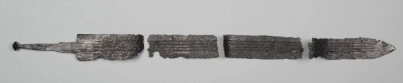 Miecz żelazny z miedzianą inkrustacją wyobrażającą Marsa i Viktorię, stanowi element wyposażenia ciałopalnego pochówku złożonego prawdopodobnie w popielnicy. Odkrycia dokonano w 1959 roku przypadkowo w czasie prac rolnych. Miecz jest obosieczny, z głownią prostą, zaopatrzoną w 4 struziny, rękojeścią symetryczną i zwężającym się trzpieniem zakończonym profilowaną płytką. Głownię zdobi u nasady miedziana inkrustacja - przedstawienie figuralne bóstw: Marsa i Victorii. Dla uwidocznienia szczegółów rysunku inkrustacja uzupełniona jest punktowaniem i liniami rytymi. Miecz był rytualnie pogięty, obecnie składa się z czterech części. Ten typ miecza używany był przez ciężkozbrojną jazdę rzymską. 
Typ VIII/3 wg. Biborskiego 
Wymiary dodatkowe: grub. 0,7-0,8 cm; 1,8x2,0 cm (wymiary płytki)