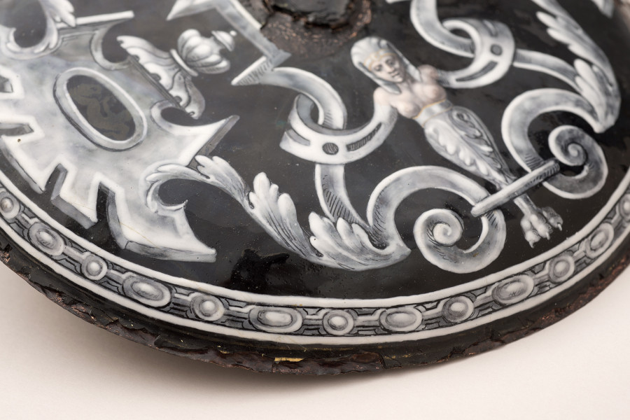 detal zewnętrznej strony patery - fragment dekoracji z kariatydą, na czarnym tle biało szara dekoracja po prawej góry gryfy z popiersiem nagiej kobiety po lewej fragment palmety z dekoracją en grisaille, wokół dekoracja z elementami owalnymi.