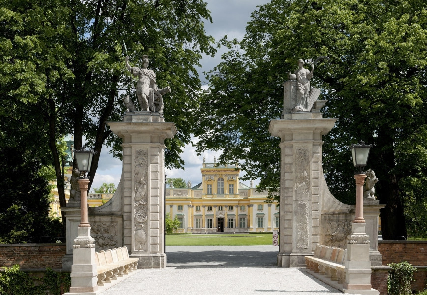Widok na Bramę Główną od strony Przedpola, w tle widoczny pałac. Po lewej i prawej na przyporach rzeźby kolejno niedźwiedzia i psa. Łączące się niewielkim łukiem z wysokimi filarami. Na filarach widoczne rzeźby. Na lewym – Mars, a na prawym – Pax. Przęsła metalowe otwarte. Do bramy prowadzi krótki brukowany most, flankowany dwiema kolumnowymi latarniami. W tle drzewa.