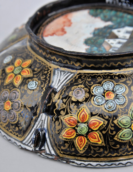 fragment zewnętrznej strony czarki - na czarnym tle, złocona arabeska i kwiaty o wypukłych płatkach, widoczny fragment dna, pejzaż z domkami, na tle grupy drzew.