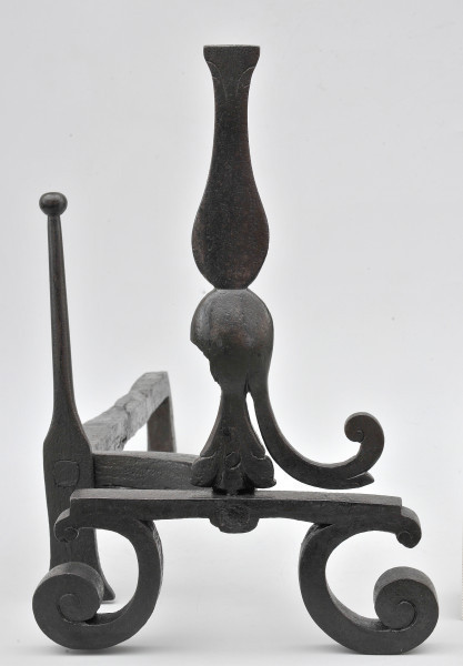 Ujęcie z przodu. Na pierwszym planie pionowy trzpień. Poniżej zwężenia na trzpieniu z prawej strony odchodzi w dół wygięte ramię. Po lewej stronie widoczny ubytek. Trzpień osadzony na płaskiej płytce, od której odchodzą wygięte stopki. Nieco z tyłu, na lewo od trzpienia, widoczny smukły szpikulec. Szpikulec jest połączony wygiętym prętem z przodem. Za szpikulcem pręt odchodzi na drugi plan. Obiekt w całości czarny, lekko błyszczący.