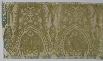 Pas tkaniny z motywami roślinnymi w kolorze żółto-zielonym. Na górze i na dole odbarwione na niebiesko pasy. Po lewej przyszyty jest materiał w kolorze niebieskim. Widoczne pionowe szwy. bryt Wil.Wn.133/3 - fragment, awers; ściana północna