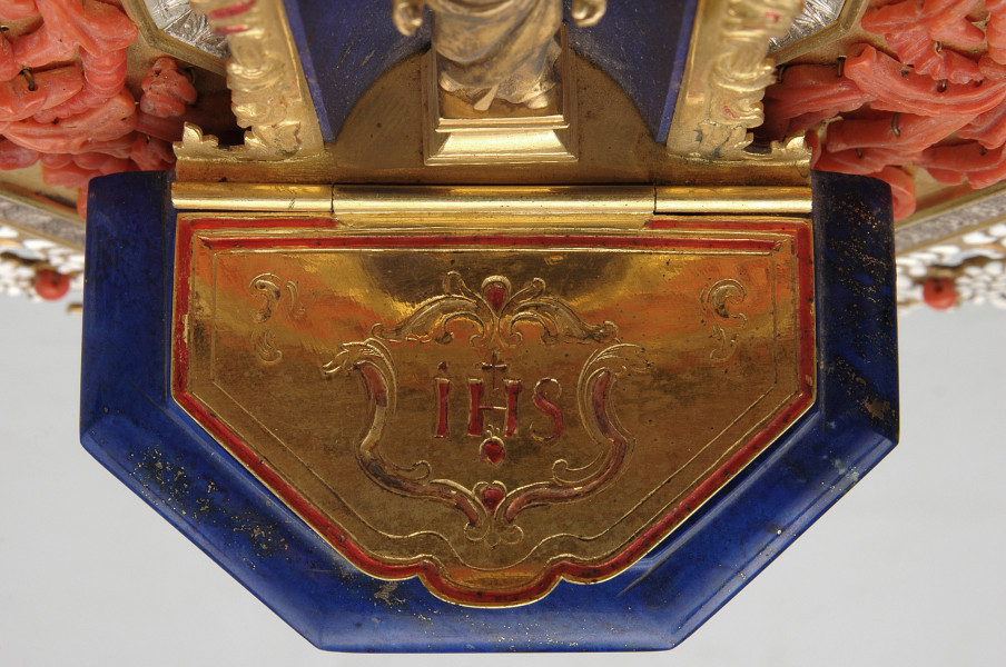 kropielniczka z brązową pokrywką, na której grawerowane IHS. Widok z góry na kropielnicę zamkniętą pokrywką z napisem IHS.