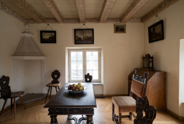 inwentaryzacja wystroju wnętrz, ściana północna, od góry belkowany sufit, po środku na drugim planie ściana z oknem, w lewym rogu kominek, na pierwszym planie stół drewniany na nim misa z owocami, w prawym rogu stoi zamknięty sekretarzyk oraz krzesło.