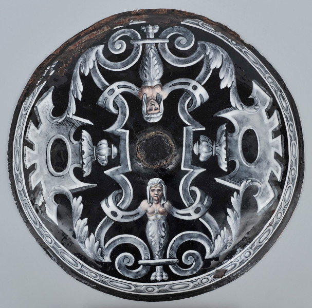 zewnętrzna strona patery okrągła, na czarnym tle biało szare zdobienia symetryczne, na dole i u góry gryfy z popiersiem nagiej kobiety, pierwsza pionowo druga odwrócona do góry nogami w lustrzanym odbiciu, po bokach palmety z dekoracją en grisaille.