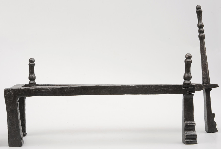 Strona czwarta. Widok z boku. Podstawka na opał wykonana z pręta, układającego się w figurę trapezu. Wsparty na czterech nogach. Nad nogą po prawej z tyłu wysoka sterczyna. Dwie niższe sterczyny nad lewą nogą z tyłu i prawą nogą z przodu. Noga pod wyższą sterczyną wysunięta bardziej w prawo.