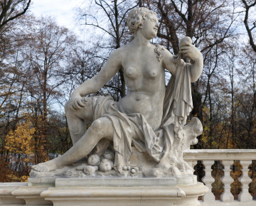 Ujęcie od strony pierwszej. Rzeźba w kolorze szarym. Postać kobiety siedzi na konarze drzewa po prawej. Tułów ustawiony przodem do widza, nogi ustawione z lewej strony a głowa skierowana w prawo i lekko w górę. Kobieta naga, tkaniny luźno leżą na jej udach oraz lewym ramieniu. W lewej dłoni, uniesionej w górę, trzyma jabłko. W drugiej ręce, opartej o prawe kolano, trzyma podłużny owoc. Włosy spięte w kok opadają na lewy bark kobiety. Pod nogami i konarem leżą rozrzucone owoce. W tle widoczne drzewa parkowe.