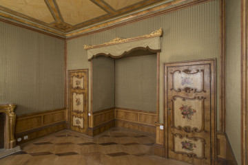 dekoracja tekstylna ściany W 66T0003, narożnik południowo-zachodni,  na ścianach obicie tekstylne o motywach pionowych pasów zielono-złotych u dołu cokół na wzór boazerii, po prawej wnęka ozdobiona złotą listwą i lambrekinem w kolorze ściany, po obu stronach wnęki dekorowane drzwi.