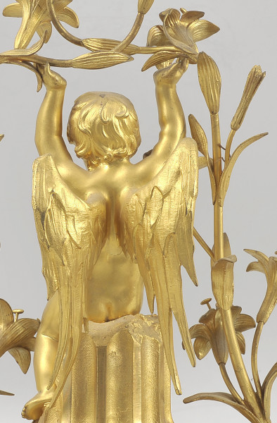 ujęcie z tyłu - fragment. Zbliżenie na postać chłopca. Na pierwszym planie widoczne skrzydła o długich wąskich lotkach, na drugim – pofalowana fryzura i pędy lilii.