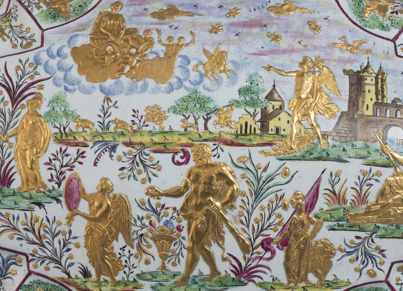 ujęcie z góry - fragment (sceny mitologiczne) wieczko. Pejzaż na pierwszym planie trzy złote postacie, w tle zabudowania w formie zamku mostu arkadowego i rzeki, po lewej stronie postać kobieca stojąca przy roślinie, w lewym górnym rogu rydwan na chmurze, po prawej stronie postać kroczącego mężczyzny ze skrzydłami.