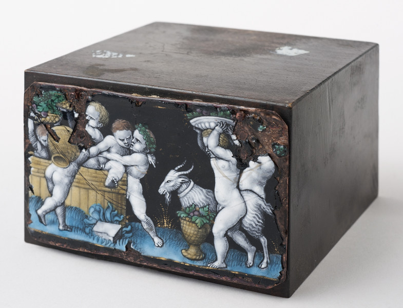 ujęcie ¾, widok z boku od góry, ukośnie ułożony drewniany klocek z plakietą na lewej ściance. Plakieta przedstawia scenę z puttami zajętymi winobraniem.