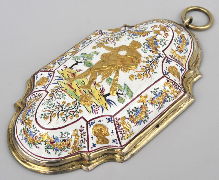 ujęcie 3/4, widok z góry na oprawę w kształcie plakiety zbliżonej do owalu o zaokrąglonych węższych bokach, z czterema półokrągłymi wcięciami na szerszych. Wypukły wierzch pokryty białą emalią, całość podzielona czerwoną cienką ramką na mniejsze sceny na skośnych elementach i scenę główną w centralnej części. Boczne sceny popiersia złote i kolorowe ornamenty roślinne, w środku herkules na tle ogrodu. W prawym górnym rogu umocowane ruchome kółko.