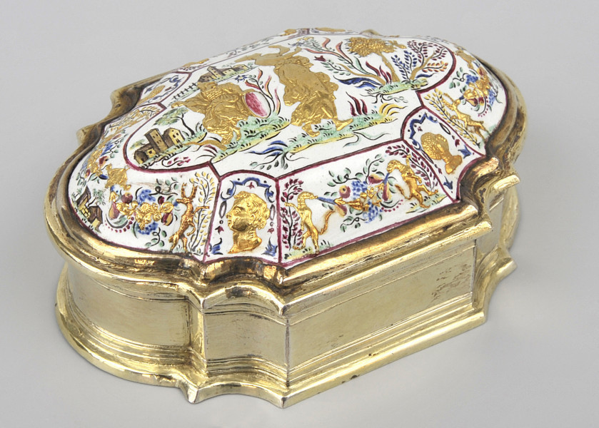 ujęcie 3/4. Ujęcie z góry, wieczko wypukłe bogato zdobione, na białym tle podzielone czerwoną cienką ramką na mniejsze sceny na skośnych elementach i scenę główną w centralnej części. Boczne sceny popiersia złote i kolorowe ornamenty roślinne, w środku pejzaż dwie złote postacie z kolorowymi roślinami. Bok puzderka złoty o zaokrąglonych węższych bokach, szersze boki z czterema półokrągłymi wcięciami.
