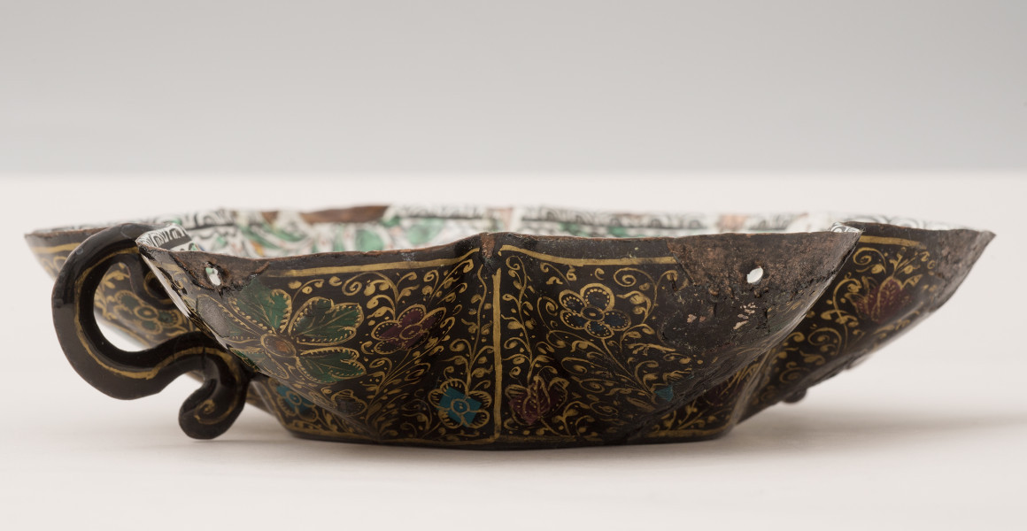ujęcie z boku. Boki zewnętrzne, pokryte czarną emalią, złoconą w arabeski i kwiaty, po lewej stronie ucho w kształcie litery s, widoczne uszkodzenia.