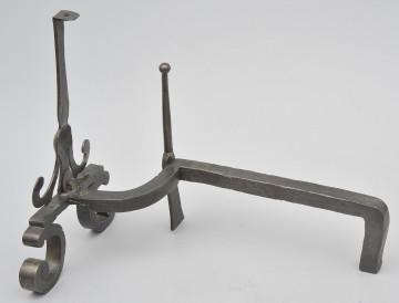 Ujęcie 3/4. Widok z boku, lekko z tyłu i od góry, z przodem po lewej stronie. W większości pręt prosty, bliżej przodu wygięty w lewo. W miejscu wygięcia smukły szpikulec. Pręt łączy się z przednią częścią obiektu przy metalowej płytce. Powyżej niej pionowy trzpień. Poniżej zwężenia na trzpieniu odchodzą dwa wygięte ramiona. Od płytki odchodzą wygięte stopki. Obiekt czarny i brązowy od rdzy.