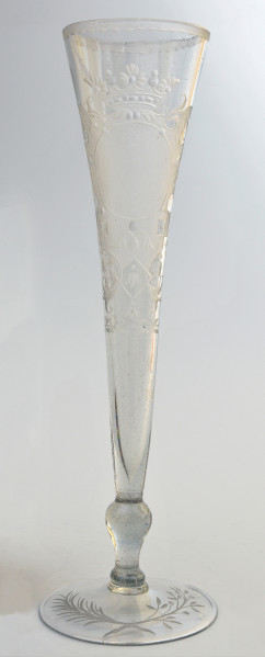 strona pierwsza. Całościowo ukazany smukły kielich, lejkowato rozszerzający się ku górze. Na okrągłej stopie skrzyżowane dwie gałązki - lauru i palmy. Wyżej tralkowata nóżka, łącząca stopę z czaszą. Bogata dekoracja z ukoronowanym polem herbowym zajmuje większą część czaszy.