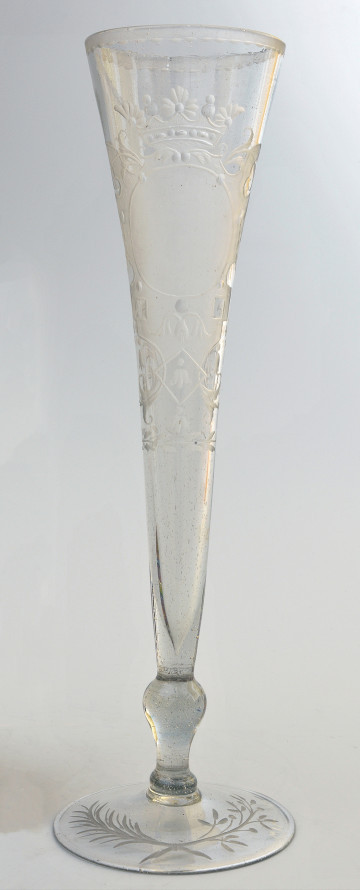 strona pierwsza. Całościowo ukazany smukły kielich, lejkowato rozszerzający się ku górze. Na okrągłej stopie skrzyżowane dwie gałązki - lauru i palmy. Wyżej tralkowata nóżka, łącząca stopę z czaszą. Bogata dekoracja z ukoronowanym polem herbowym zajmuje większą część czaszy.