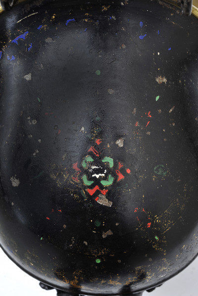 Fragment wazy hełmowej z dekoracją malarską - ujęcie z góry. Zbliżenie na dekorację w formie rozety. W znacznej części wytarta, wyraźnie zachował się niewielki fragment. Kolory zielony i czerwony na czarnej ścianie.