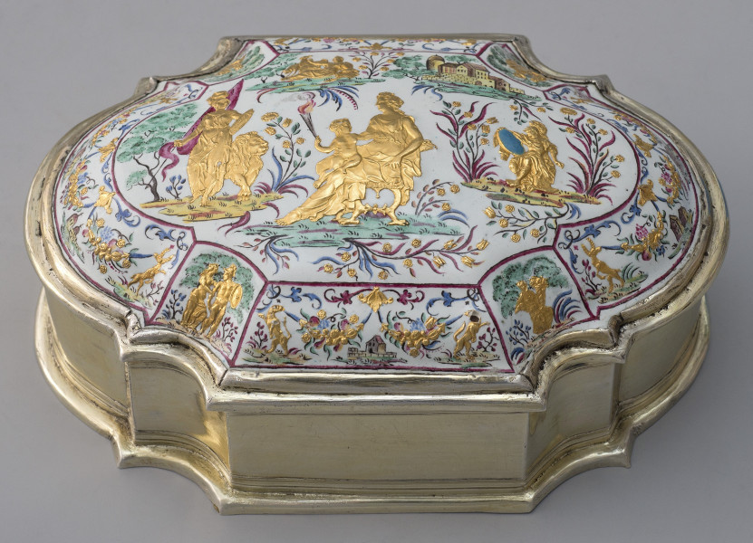 ujęcie lekko z góry, wieczko wypukłe bogato zdobione, na białym tle podzielone czerwoną cienką ramką na mniejsze sceny na skośnych elementach i scenę główną w centralnej części. Boczne sceny rodzajowe, leżąca po środku psy trzymające girlandy z kwiatów z zabudowaniami w tle, po prawej i lewej sceny rodzajowe złote postacie,  po bokach jelenie trzymające girlandy. Duża scena w centralnej części wieka, pejzaż cztery złote postacie, z lewej kobieta ze sztandarem i lwem po środku kobieta siedząca z dzieckiem na kolanach po prawej postać w zbroi z niebieską tarczą, w tle zabudowania. Bok puzderka złoty o zaokrąglonych węższych bokach i półokrągłymi wcięciami.