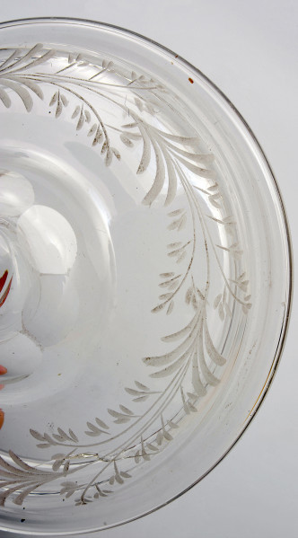 ujęcie z góry na fragment dolnego wybrzuszenia pokrywy.  Powierzchnia pokrywy jest dekorowana motywem roślinnym. Zgodnie z obwodem pokrywy biegnie, matowo rytowany otok z gałązek o drobnych listkach.