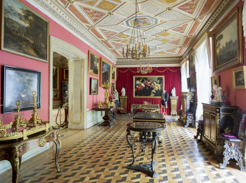 ściana zachodnia, w tle ściana zakryta czerwoną drapowana tkaniną i duży obraz, podłoga z wzorem geometrycznym, przy ścianie po prawej komody i krzesła, po prawej komody z złotymi kandelabrami, na ścianie po prawej duży portal ze zdobionym u góry gzymsem, bogato zdobiny sufit. Na różowych ścianach obrazy.