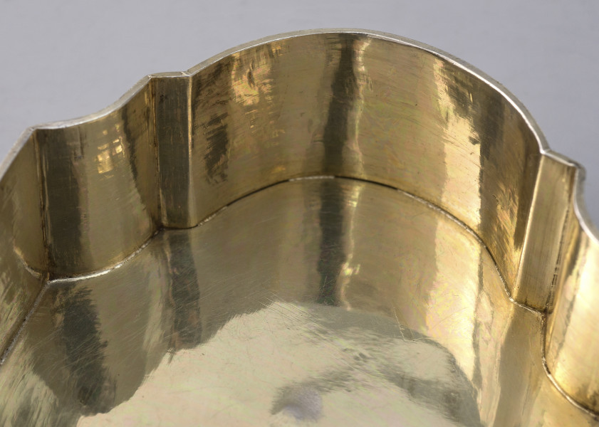 fragment wnętrza puzderka, widok na załamanie ścianki bocznej zaokrąglonej z półokrągłymi wcięciami oraz półowalnym wypustem, dno gładkie widoczne odbicie ścianki bocznej w tafli dna.