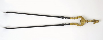 awers. Szczypce kominkowe ułożone poziomo, rączką skierowane w prawo. Ramiona lekko rozwarte, czarne. Górna część ramion, przegub oraz rączka złocone, pokryte bogatą wypukłą dekoracją.