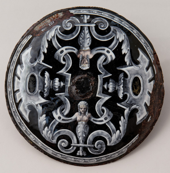zewnętrzna strona patery okrągła, na czarnym tle biało szare zdobienia symetryczne, na dole i u góry gryfy z popiersiem nagiej kobiety, pierwsza pionowo druga odwrócona do góry nogami w lustrzanym odbiciu, po bokach palmety z dekoracją en grisaille. Duże uszkodzenia emalii, lewy górny róg napis Wil.207.