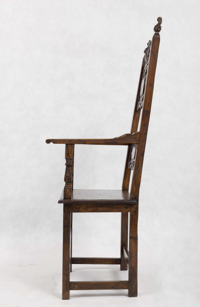 Fotel drewniany z  siedziskiem i oparciem drewnianym bez wyściełania, na prostych nogach z czterema łączynami. Nogi tylne przechodzą w ramiaki boczne oparcia. Oparcie prostokątne, lekko odchylone do tyłu. Zaplecek ażurowy złożony z dwóch bogato rzeźbionych desek:
- górna w ornamenty wolutowe wokół środkowago owalnego medalionu, z ozdobnie wyciątą dolną krawędzią i wyodrębnionym zwieńczeniem w kształcie przełamanego tympanonu z centralnym kartuszem
- dolna - węższa, powtarza główny motyw zdobienia.
Poręcze graniaste zakończone małymi wolutkami, u nasady rzeźbione liście akantu, podpórki w środkowej części rzeźbione. Płyta siedzenia prostokątna z rzeźbionym fartuchem z przodu. Łączyny boczne i tylna - graniaste, łączyna przednia w postaci deski o ozdobnym wykroju, rzeźbionej w ornamenty wolutowe.