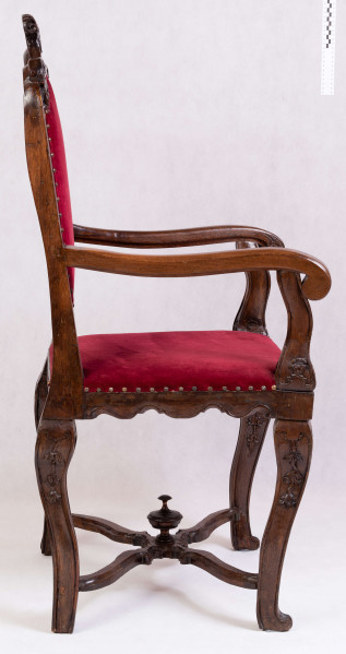 S/Mb/132/ML - Fotel z tapicerowanym siedziskiem i oparciem, na czterech nogach wygiętych kabriolowo, połączonych skrzyżowanymi trawersami. Oskrzynienie prostokątne z fartuchem wysiętym w zęby przypominające lambrekin. Oparcie ażurowe, prostokątne, od góry zamknięte faliście z wolutowym szczytem pośrodku, deska dolna wycięta analogicznie do fartucha oskrzyni. Poręcze drewniane wyrastają z ramiaków bocznych oparcia, lekko wygięte, zakończone wolutami. Podpórki poręczy profilowane i rzeźbione w dolnej części.podobnie opracowanwe nogi, rzeźbione w liscie akantu u nasady, połączone wolutowymi trawersami z okrągłą sterczynką na skrzyżowaniu. Tapicerka na pasach, pokrycie bordowym aksamitem, na brzegach mosiężne gwoździe






  