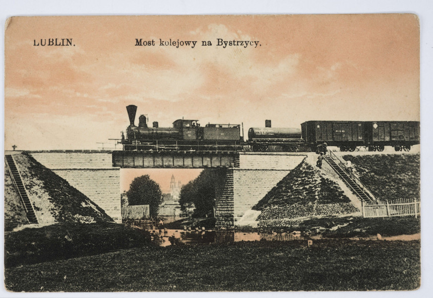Pocztówka barwna (w tonacji różowej) z widokiem mostu kolejowego na rzece Bystrzycy w Lublinie
AWERS: Widok na most kolejowy murowany jednotorowy (?) z przejeżdżająca lokomotywą parową i wagonami. Poniżej, pod wiaduktem, rzeka. W głębi fragment zabudowy miejskiej. Po obu stronach nasypy ziemne ze schodami. U góry nadrukiem w kolorze czarnym napisy informacyjne.
REWERS: Czarna linatura. Wyznaczone pole na adres i korespondencje. Nadruk w kolorze czarnym z informacją o nakładcy umieszczony poziomo pośrodku karty. Brak korespondencji oraz śladów obiegu pocztowego. W p. g. rogu odcisk (w kolorze fioletowym) okrągłej pieczęci tuszowej 
