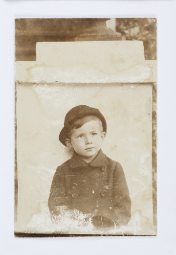 W kapelusiku na głowie, w palcie z dwurzędowym zapięciem.