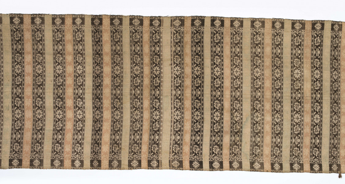 Pas kontuszowy dwustronny.
Ornament: 
głowy-trzy motywy stylizowanego kwiatu  goździka (każdy o czterech zgeometryzowanych płatkach)
wciąż pasa- poprzeczne pólka o kolejnych powtarzajacych się sekwencjach motywów:
-ciąg palmetek
-stylizowane kwiaty na tle łososiowym
-stylizowane kwiaty na tle zielonm
obrzeżenie- nieznacznie wyodrebnione dekorowane rozetką
Frędzla wysnuta z osnowy