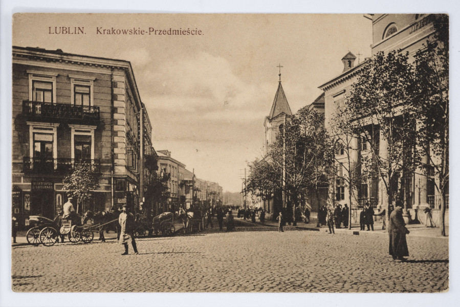 Pocztówka w sepii z widokiem placu Łokietka, ulice Krakowskie Przedmieście, kościoła pw. Św. Ducha i Nowy Ratusz w Lublinie. 
AWERS: Ulica wybrukowana. Na chodnikach liczni przechodnie. Po lewej stronie przy pierwszej kamienicy stojąca przy placu dorożka konna z woźnicą. Przy ulicy i przed fasadą Ratusza szereg drzewek liściastych. Na pierwszym planie na placu po lewej i po prawej przechadzający się dwaj mężczyźni zwróceni do widza. 
REWERS: Linatura w kolorze czarnym. Wyznaczone pole na korespondencję i adres. U góry drukiem napis informacyjny w językach francuskim, polskim i rosyjskim. Przy lewej krawędzi pola tekstowego nadruk z informacją o wydawcy. Brak śladów obiegu pocztowego.